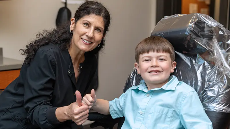 hygienist and child patient smiling with thumbs up