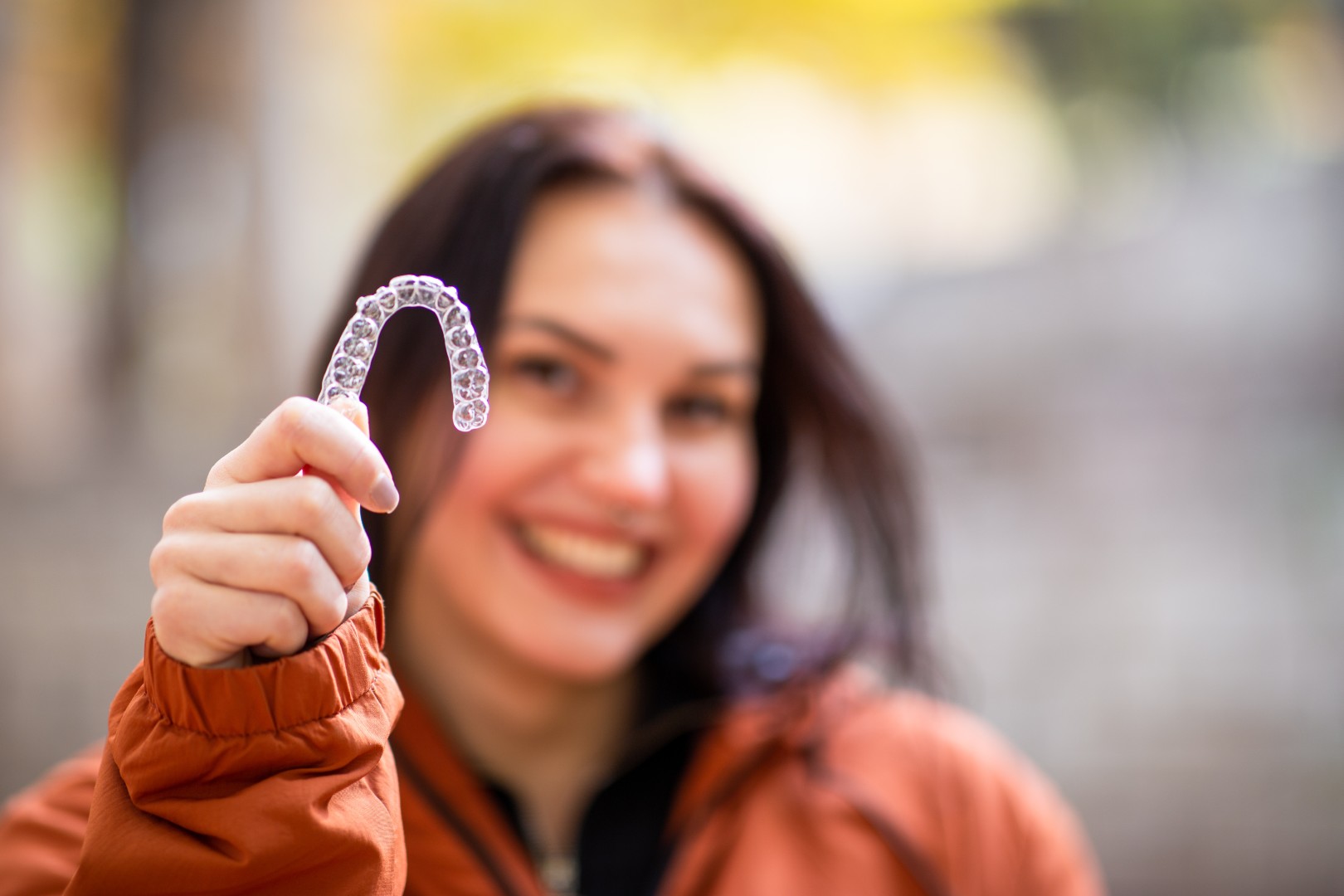 Happy young woman smiling with invisible teeth aligner during fall season at park.